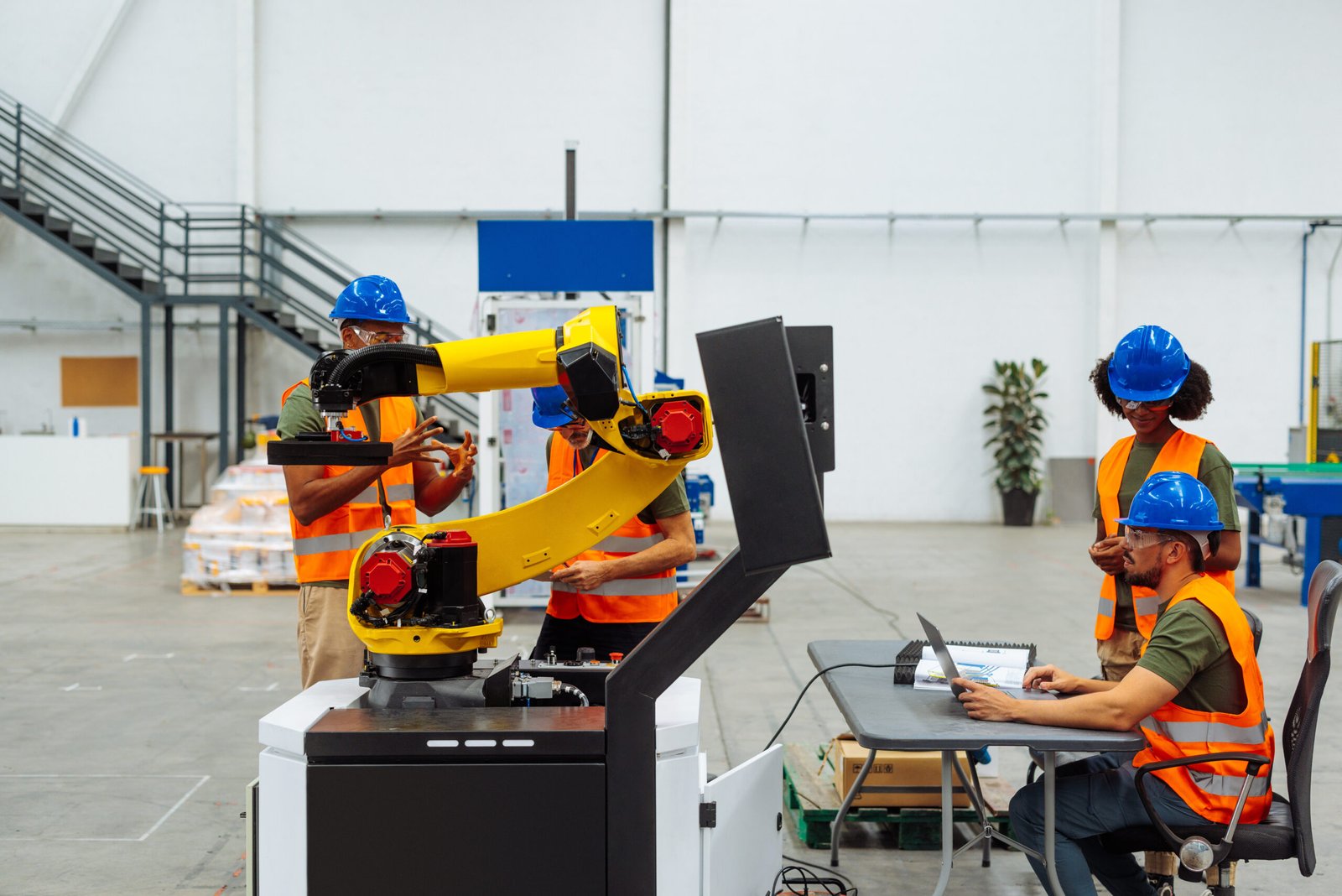 Industrial workers and engineers collaborating on Robotics Training & Automation Workforce Integration, programming a robotic arm in a factory training environment.