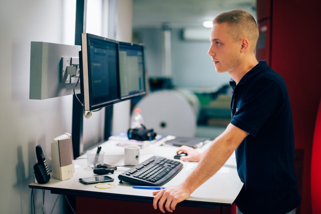 Young man operating printing press in a factory, demonstrating print workflow automation in action.